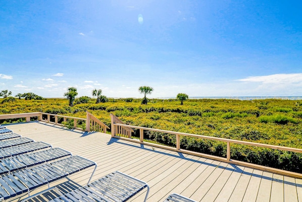 Een houten terras met lounge fauteuils en uitzicht op een verzorgd landschap met bomen en struiken.