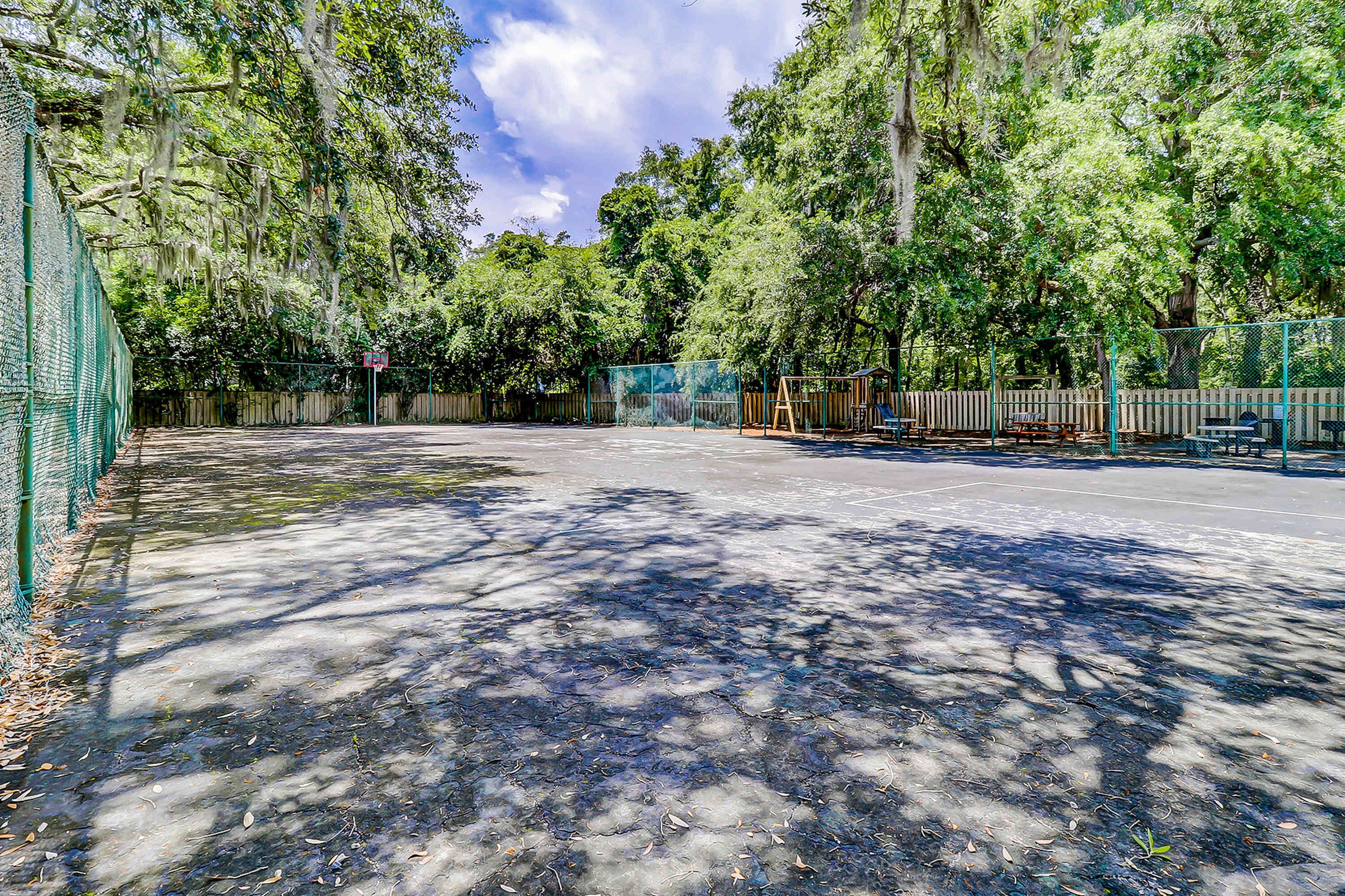 Una zona pavimentada con valla, árboles y un parque infantil.