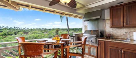 A balcony with a dining set, a ceiling fan, and a view of a lush landscape.
