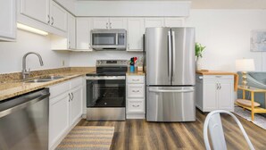 A modern kitchen with white cabinets, stainless steel appliances, and a wooden floor.