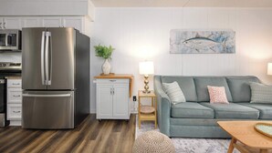 A modern kitchen with a stainless steel refrigerator, white cabinetry, a microwave, and a wooden floor.