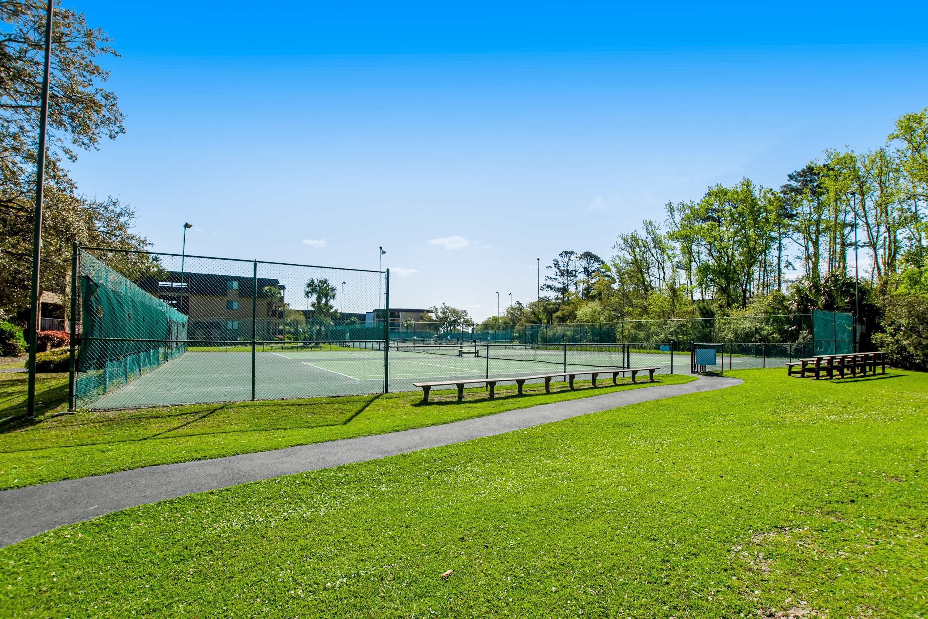 Un court de tennis entouré d’une clôture, avec des bancs et un chemin.