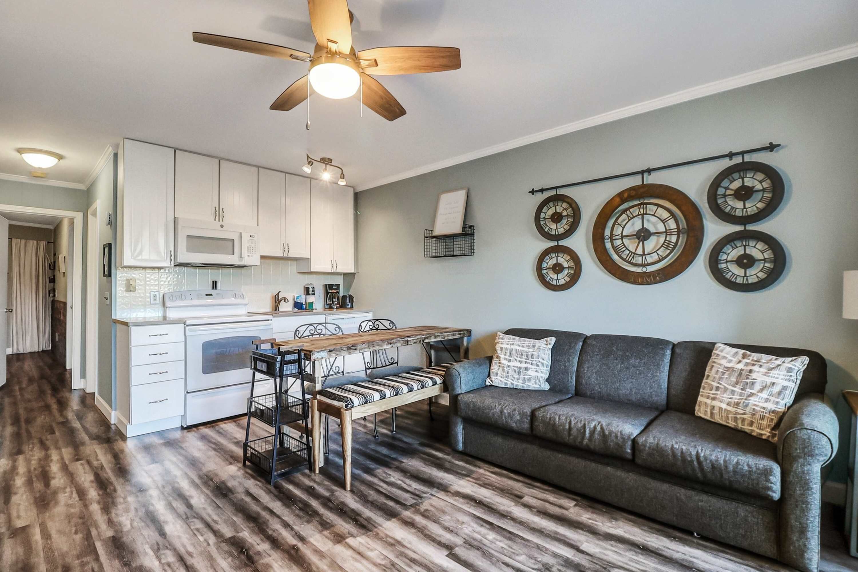 A modern kitchen with white cabinets, a wooden dining table, and a ceiling fan.