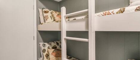 A bunk bed with patterned bedding and a white wardrobe.