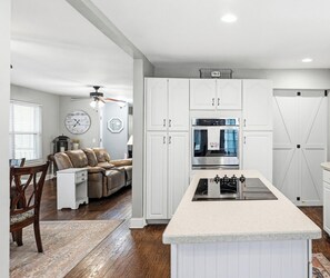 A modern kitchen with white cabinetry, a central island with an induction cooktop, and a built-in oven. - Fripp Island Coastal Haven  Sleeps 10 + Golf Cart (Fripp Island)