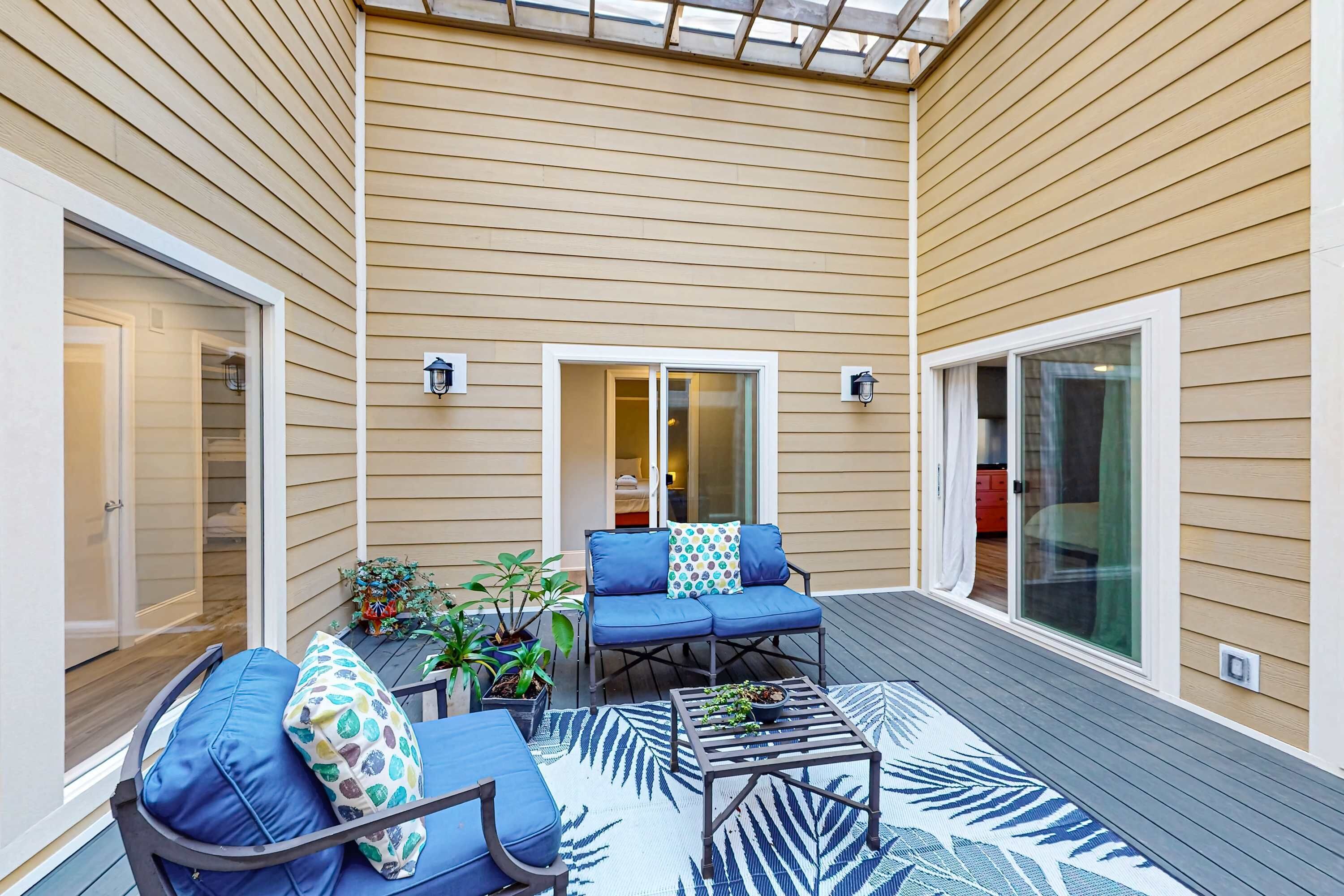 A covered patio with a blue sofa set, a coffee table, and potted plants.