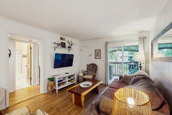 A living room with a TV, sofa, and a window with a view. - Condo 1 block from Coligny Plaza with on site pool, balcony, Washer, Dryer (Hilton Head)
