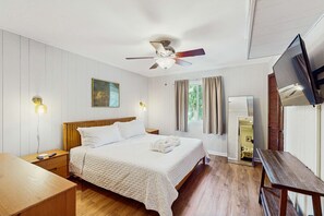 A hotel room with a bed, wooden floor, ceiling fan, bedside table, nightstand, lamp, and a TV. - Condo 1 block from Coligny Plaza with on site pool, balcony, Washer, Dryer (Hilton Head)