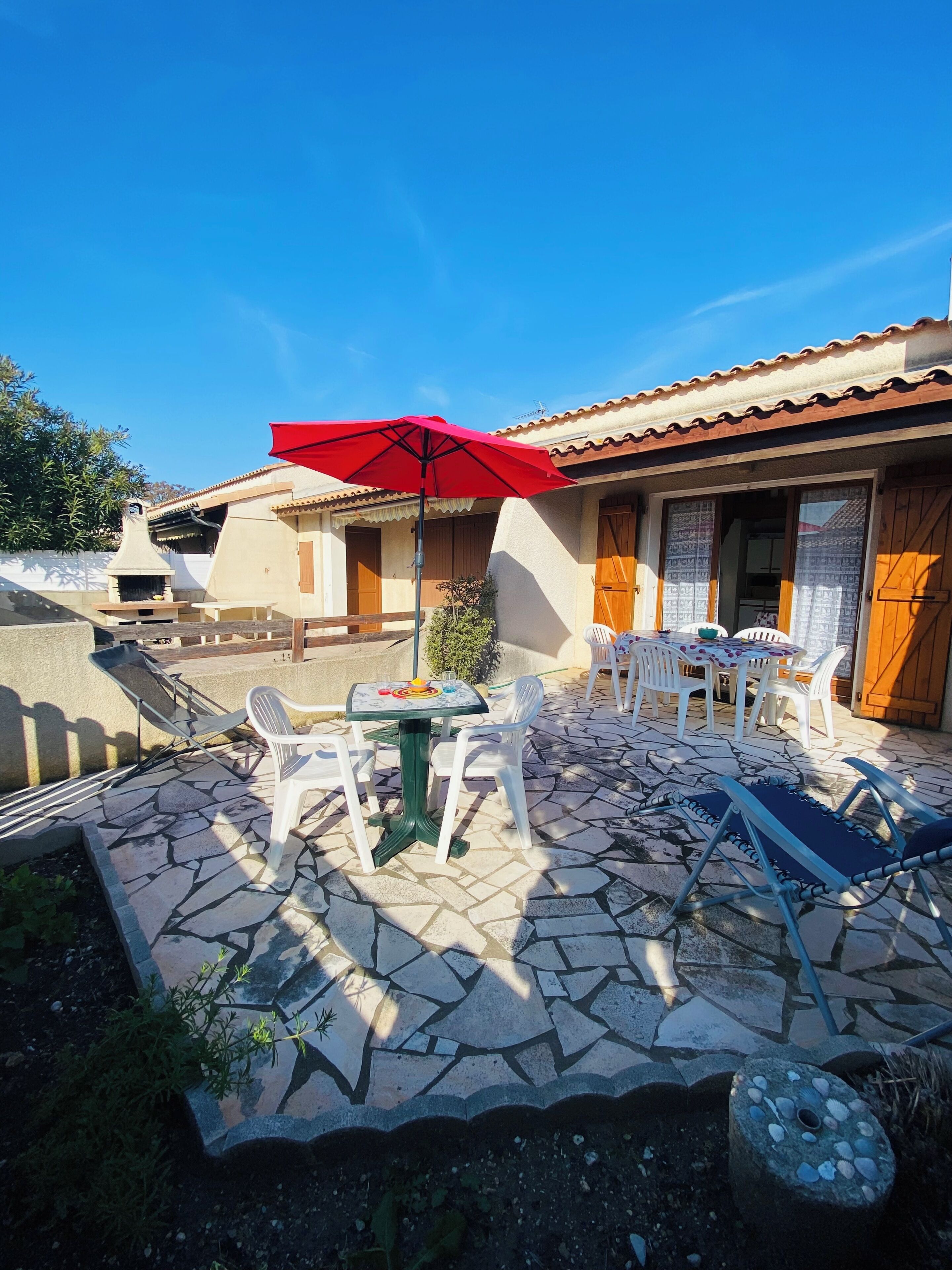 Un patio con suelo de piedra, mobiliario exterior, una sombrilla roja y un edificio tradicional con puertas de madera.