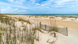 Ein Strand mit Dünen, einem Holzzaun und dem Meer im Hintergrund.