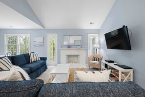 Ein Wohnzimmer mit einer Couch, einem Couchtisch, einem Kamin, einem Fernseher und einem Bücherregal.