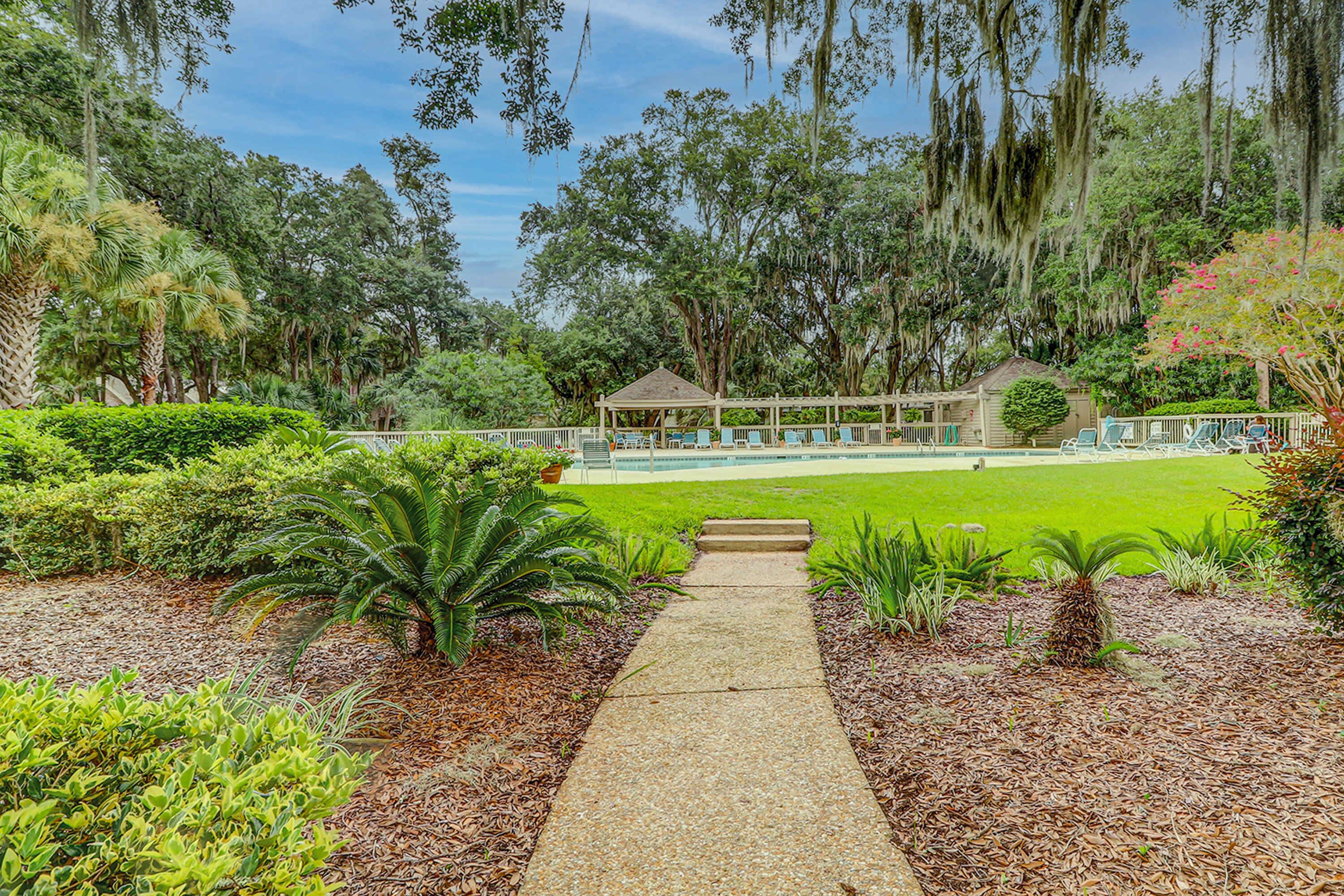 A pathway leading to a gazebo surrounded by lush greenery and a pool.
