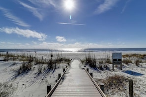 A wooden boardwalk leading to a beach with a sandy path, a clear sky, and a signboard. - Beautiful updated condo- On-site pool, blocks from beach and Coligny Plaza (Hilton Head)