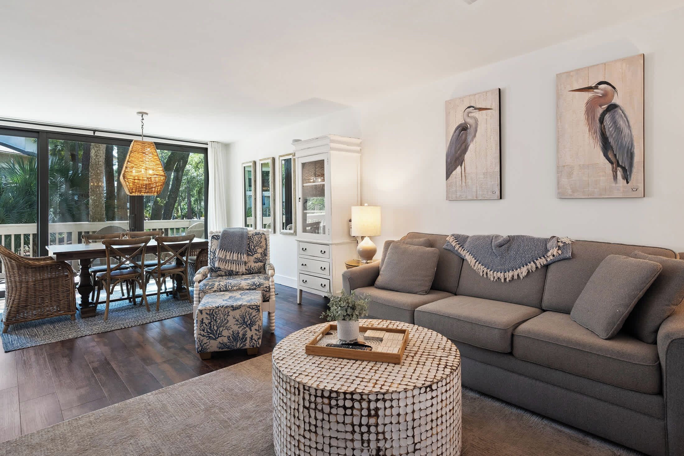 A spacious living room with a grey sofa, a round coffee table, and a dining area with wicker furniture.