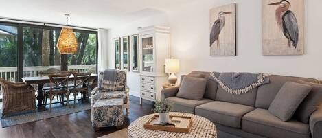 A spacious living room with a grey sofa, a round coffee table, and a dining area with wicker furniture.