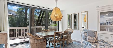 A dining area with a table and chairs, a hanging light fixture, and a view through a glass door to the outdoors.
