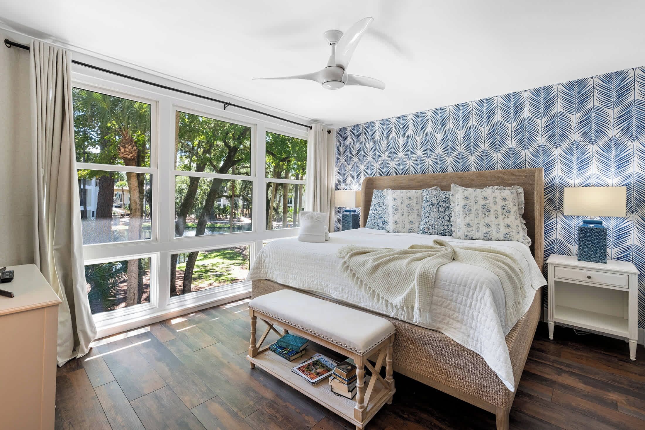 A bedroom with a large window, a bed, a bedside table, and a bench.