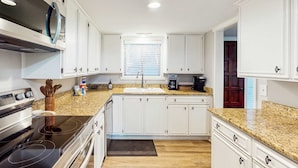 A modern kitchen with white cabinets, a granite countertop, a built-in oven, and a window with blinds.