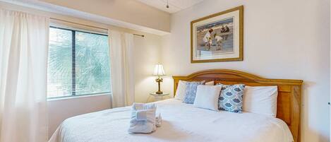 A hotel room with a bed, a ceiling fan, a window with curtains, a bedside lamp, and a framed picture on the wall.