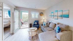 A living room with a sofa, armchair, and a small table. There is a balcony with a chair and a table. - Beach condo with balcony, pools, & hot tub- near golf & beach (Hilton Head)