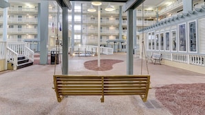 A multi-level atrium with a central swing area, a covered seating area, and a view of the building's exterior balconies. - Beach condo with balcony, pools, & hot tub- near golf & beach (Hilton Head)
