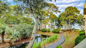 A pathway leading to a body of water, surrounded by trees and a building. - 2nd floor Coastal Condo, pool, tennis and close to beach (Hilton Head)