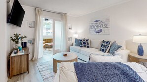 A modern living room with a sofa, coffee table, and a flat-screen TV mounted on the wall. - 2nd floor Coastal Condo, pool, tennis and close to beach (Hilton Head)