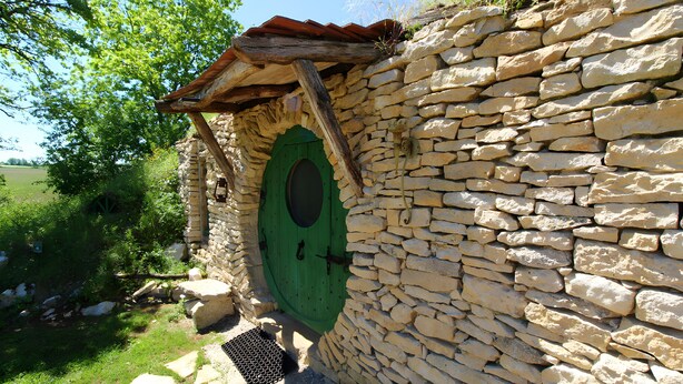 Un mur de pierre avec une porte verte, un toit en bois et un chemin pavé de pierres.