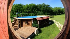Une terrasse en bois avec une piscine bleue, une échelle et un mur en pierre.