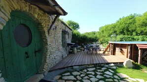Un bâtiment en pierre avec une porte verte, une terrasse en bois et un chemin en pierre.