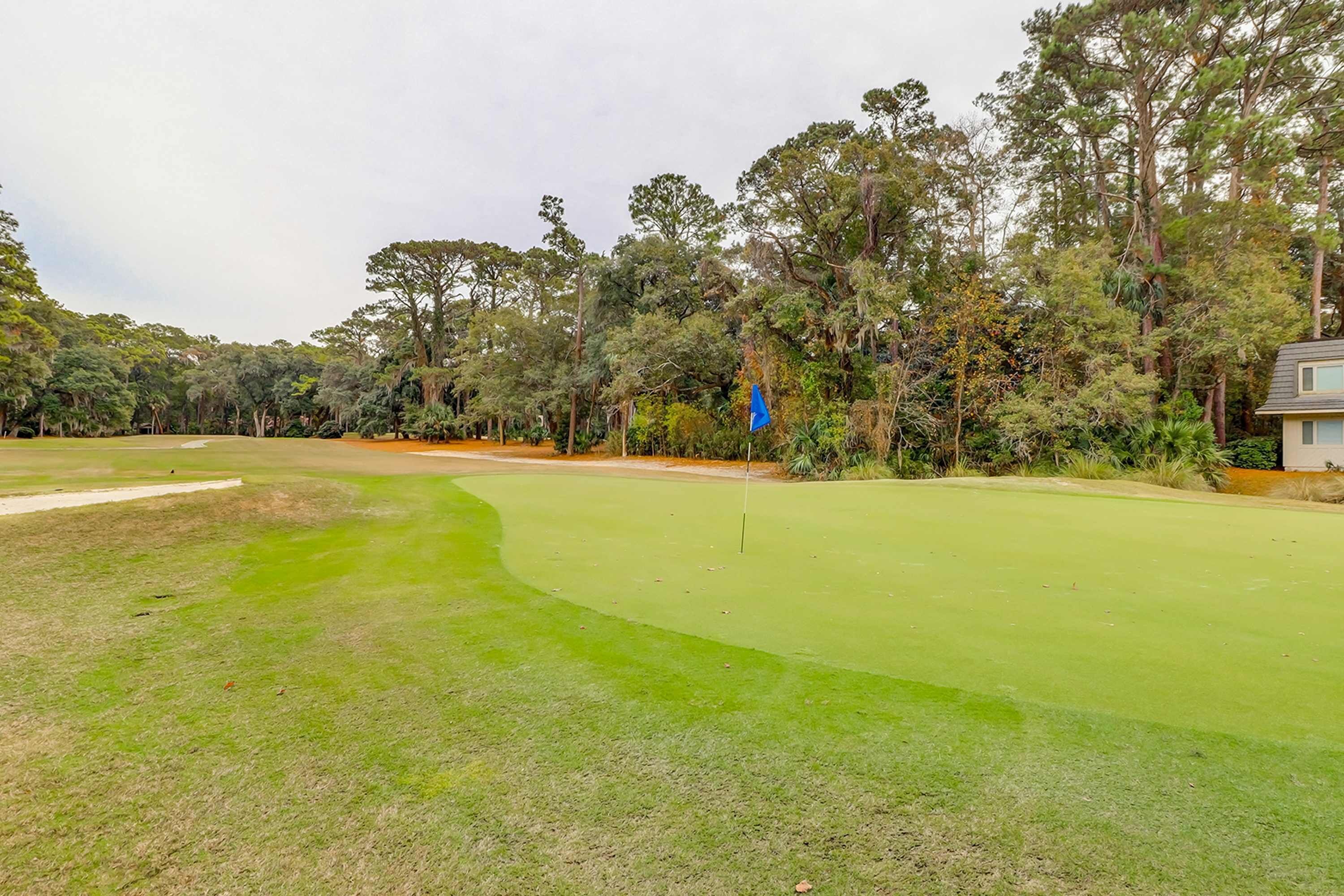 A golf course with a flag, trees, and a building in the background.