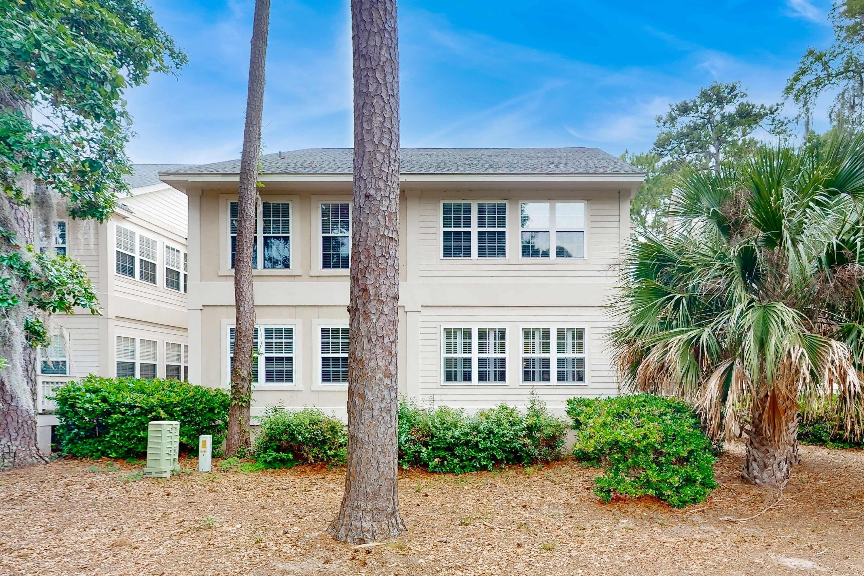 A two-story building with a symmetrical facade, multiple windows, and a well-maintained garden with trees and shrubs.