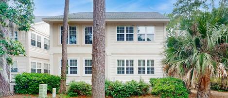 A two-story building with a symmetrical facade, multiple windows, and a well-maintained garden with trees and shrubs.