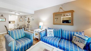 Un salon avec des canapés bleus à rayures, un coin repas avec des chaises en métal, une table blanche avec une lampe et un miroir au mur.