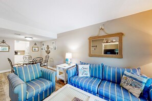 A living room with striped blue sofas, a dining area with metal chairs, a white table with a lamp, and a mirror on the wall. - Relaxing Condo with pool near Beach, Shopping & Restaurants (Hilton Head)