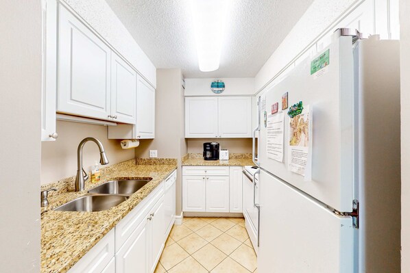 Una cocina compacta con armarios blancos, encimera de granito, pileta de acero inoxidable y refrigerador.