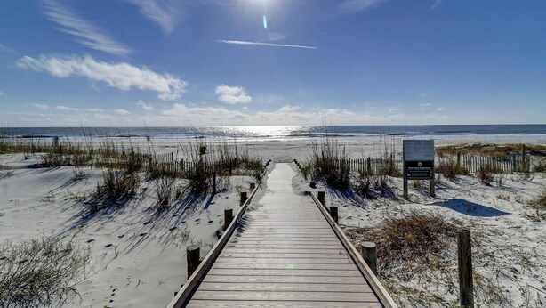 A wooden boardwalk leading to a beach with a clear sky and a signboard. - Coastal condo with private grill and shared pool, nearby beach access (Hilton Head)