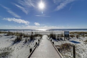 Ein hölzerner Steg führt zu einem Strand, am bewölkten Himmel steht ein Schild.