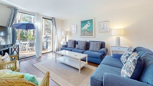 A living room with a blue sofa, a white coffee table, wicker chairs, and a TV. - Coastal condo with private grill and shared pool, nearby beach access (Hilton Head)