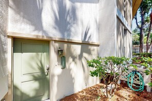 Edifici amb una porta verda, un arbre petit i una manguera.