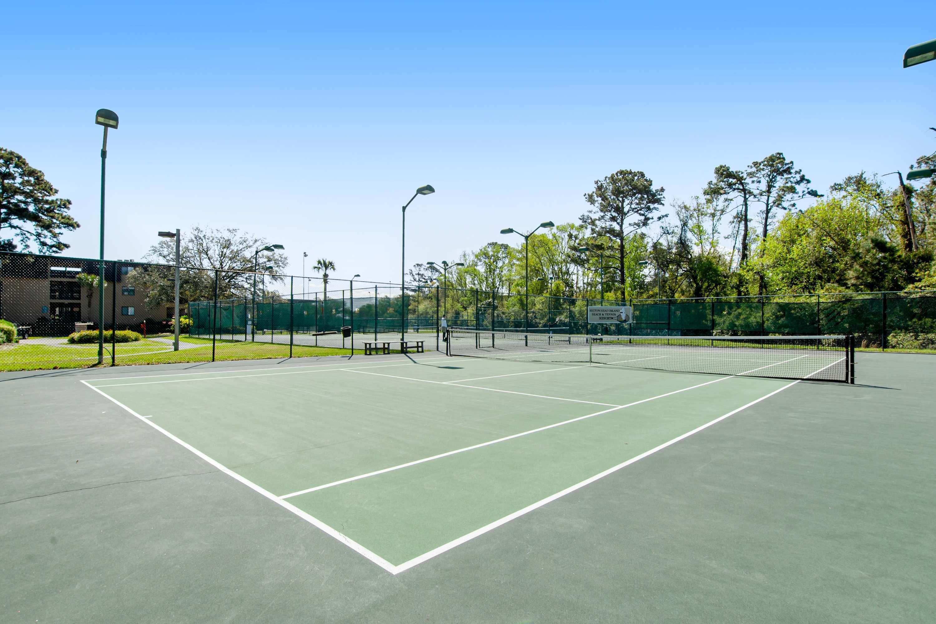 Un terrain de tennis avec un filet, entouré d’une clôture, de bancs et de lampadaires.