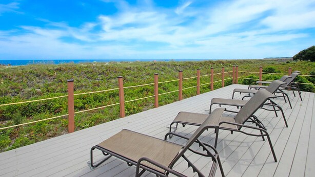 Een terras met loungebedden met uitzicht op een strand.