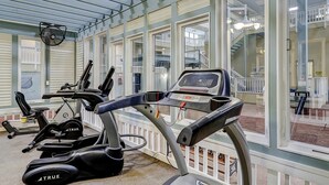 Ein Fitnessstudio mit Trainingsgeräten, großen Fenstern und Blick auf einen Balkon.