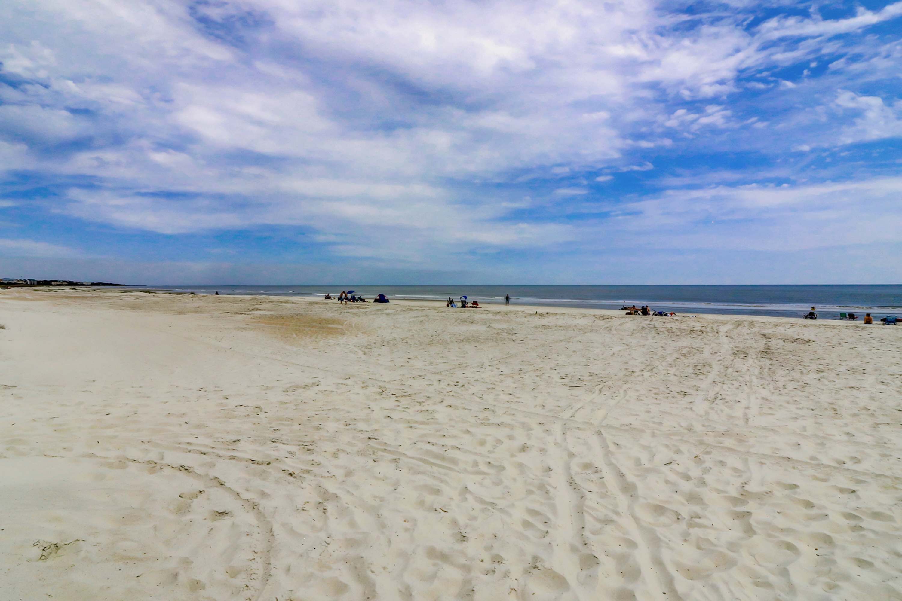 A wide sandy beach with footprints, a clear sky, and the ocean in the distance.