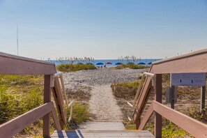 Un sendero de madera que conduce a sombrillas de playa y una playa arenosa.