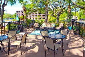 Un patio al aire libre con mesas y sillas, una piscina y un edificio al fondo.