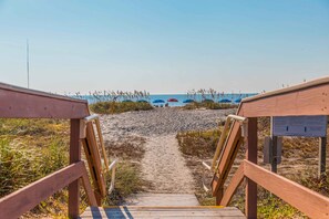 Un sendero de madera que lleva a sombrillas de playa y una playa arenosa.