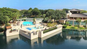 Un resort con una piscina grande, cancha de tenis y un edificio de techo inclinado.