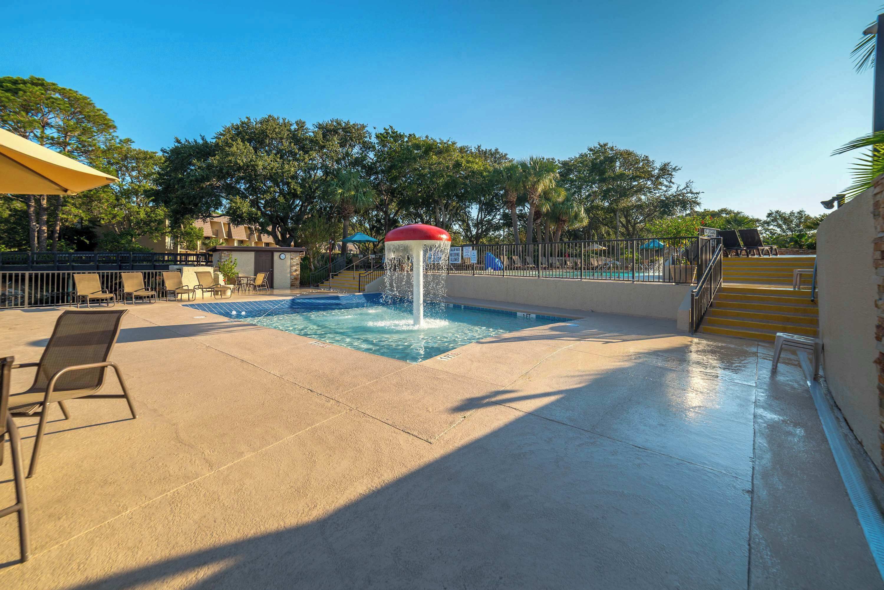 A pool area with a water feature, lounge chairs, and a staircase leading to a pool.