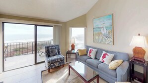 Uma sala de estar com sofá, poltrona, mesa de centro e um quadro na parede.